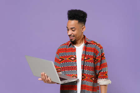 Smiling young african american guy in casual colorful shirt posing isolated on violet background...