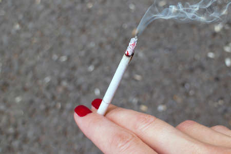Smoldering cigarette with smoke in a womans hand with nails paintedの写真素材