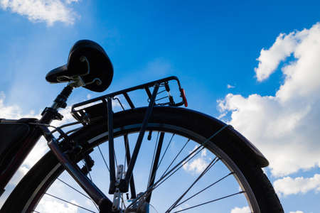 Bicycle, rear wheel and saddle against a blue sky with cloudsの写真素材