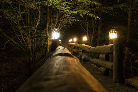 Old wooden bridge over the little stream, lit lanterns in the night.の写真素材
