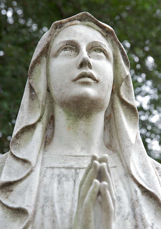 Ancient cemetary heastone of a woman in prayer looking toward heaven.  Spider webs cover the eyes giving the image a spooky and creepy feeling.の写真素材