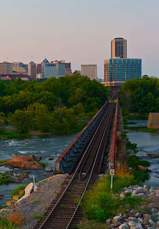 Old neglected railroad tracks leading over a river leading into a city.の写真素材