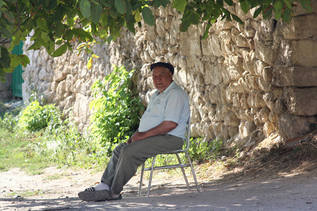 Ukraine, Bakhchisaray - September 06, 2011: Elderly man oriental appearance sitting on a chair on a city streetのeditorial素材