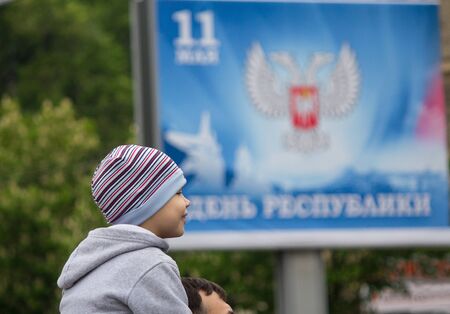 Donetsk, Ukraine -May 09, 2017: Boy on the shoulders of his father against the background of a banner calling for the celebration of the Republic Dayのeditorial素材