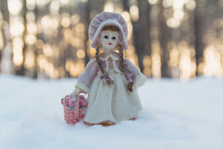 Toy girl figure with a basket of flowers in the snow-covered forestの写真素材