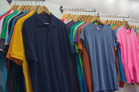 Variety of t-shirts of different colors on wooden hangersの写真素材