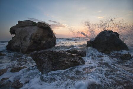 Splashing waves beat against the rocks on the beach at sunset. Crimeaの写真素材