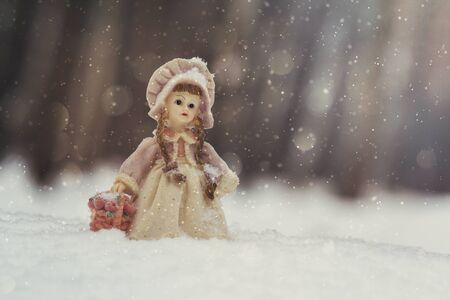 Toy girl figure with a basket of flowers in the snow-covered forestの写真素材