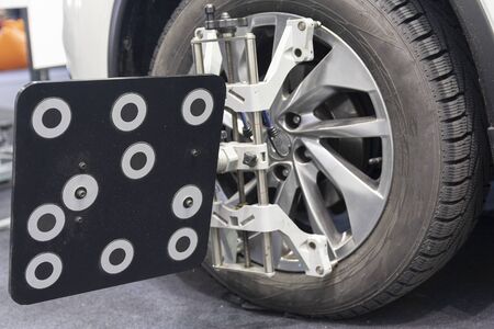 Car mechanic installing sensor during suspension adjustment and automobile wheel alignment work at...