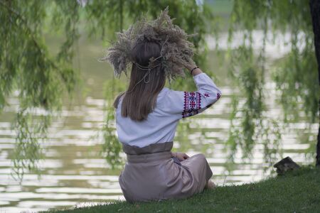 Girl in a grass wreath sits by the lake. National Slavic holiday of Ivan Kupalaの写真素材
