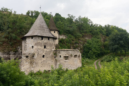 Medieval stone fort with two towers near the rock in the greenery. Kamianets-Podilskyi, Ukraine
