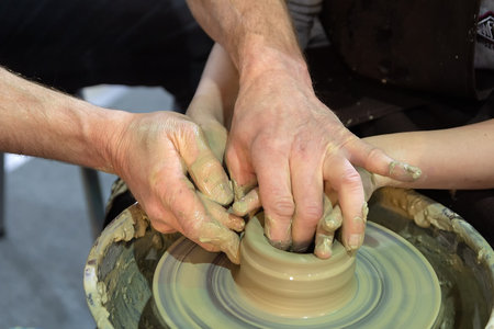 A potter teaches a child to work with clay on a pottery wheel. Craftの写真素材