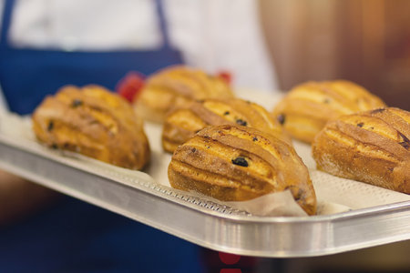 Baker carrying freshly baked crispy golden cakes on a metal tray to coolの写真素材