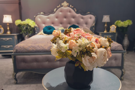 Beautiful bouquet of flowers in the foreground of a luxury classic style bedroom. Interior