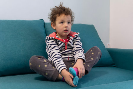 Portrait of cute curly baby sitting on sofa in room. Peopleの写真素材