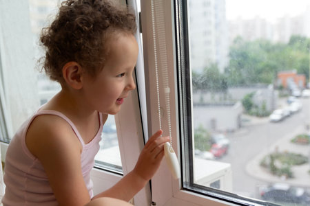 Curly child looks out the window sitting on the windowsill.の写真素材