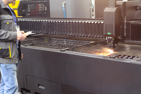 A worker operates a steel laser cutting machine at a factory. Industryの写真素材