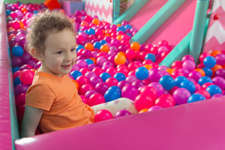 A curly-haired baby plays in a multicolored ball pool in a children's playroom. Peopleの写真素材