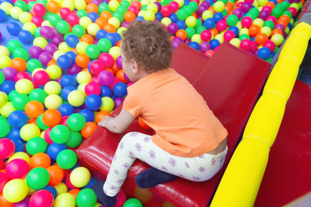 A curly-haired baby plays in a multicolored ball pool in a children's playroom. Peopleの写真素材