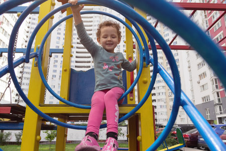 The curly child plays on the playground against the backdrop of a multi-storey building.の写真素材