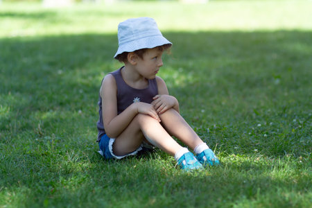 A child in a panama hat sits on the grass in the park. Peopleの写真素材