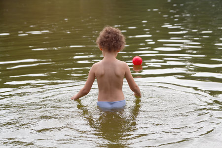 A curly child plays with a ball in the lake in the summer. Peopleの写真素材