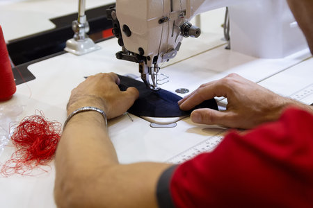 Men's hands near the sewing machine hold a cloth, in the process of sewing. Sewing, design work,...