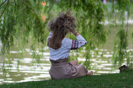 Girl in a grass wreath sits by the lake. National Slavic holiday of Ivan Kupalaの写真素材