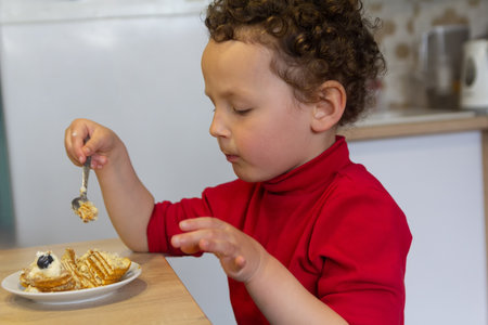 A curly child eats sitting at the home table. Peopleの写真素材