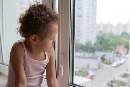 Curly child looks out the window sitting on the windowsill. Peopleの写真素材