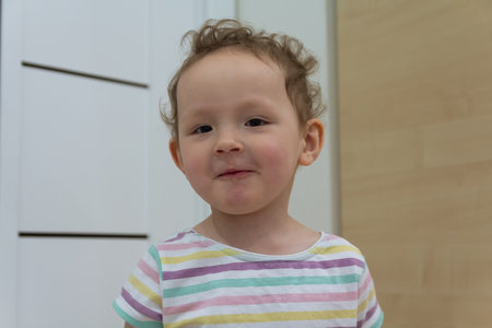 A cheerful child with curly hair stands proudly in a warm, cozy room. Peopleの写真素材