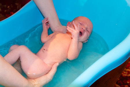 Mother bathes her baby in a blue small plastic tub. Peopleの写真素材