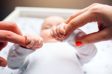 Newborn baby in the nursery. Mom and Dad are holding the baby by the hands. Close-upの写真素材