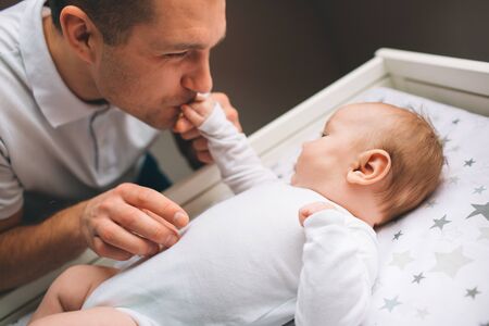 Newborn baby in the nursery. Father gently kisses and holds the babys hand.