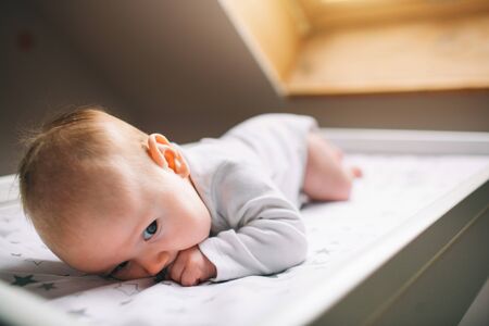 Little infant is lying on the kids table near window. There is Newborn child on the baby changing table.の写真素材