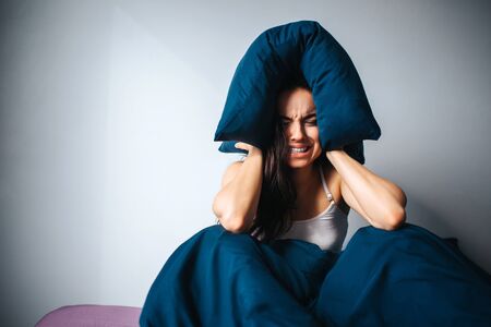 Young beautiful woman in morning bed at home. Irritated female person suffer from noise. Hold pillow...