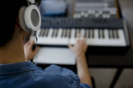 Blurred focus close-up. Male music arranger hands composing song on midi piano and audio equipment...