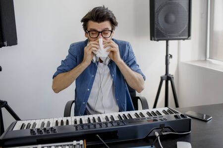 The man got sick. He blows his nose. Composer in the recording studio. music production technology, . Man is working on sound mixer in recording studio or DJ in broadcasting studio.の写真素材