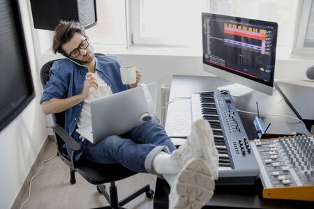 Talking on the phone and working on a laptop. Busy guy. Multitasking concept. DJ in broadcasting...