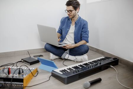 Man produce electronic soundtrack or track in project at home. Male music arranger composing song on midi piano and audio equipment in digital recording studio.の写真素材
