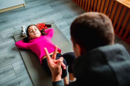 young father and his cute little daughter have ABS workout at home. Cute kid and daddy is training...