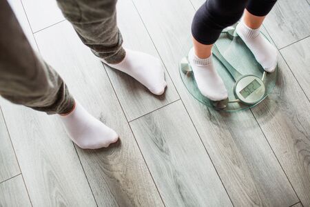 Father and daughter are weighed on indoor household scales. Funny and joyful moments having fun in...