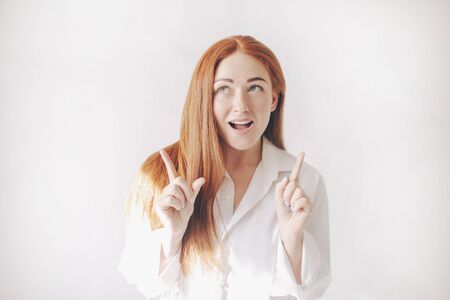 red-haired woman stand isolated on a white background in spacious oversized shirts. girl point upwards with index fingers.の写真素材