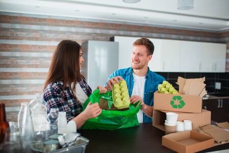 A young couple sorts trash in the kitchen. Young man and woman are sorting recyclables in the...