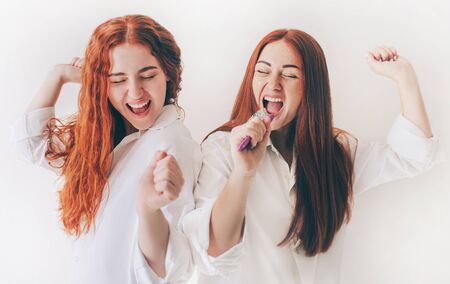 Two red-haired sisters stand isolated on a white background in spacious oversized shirts.