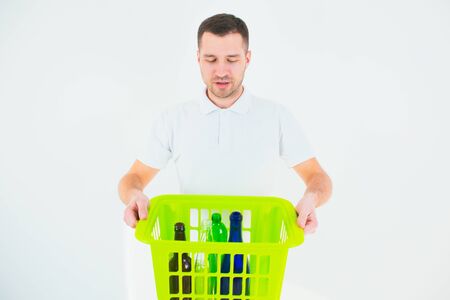 Young man isolated over white background. Guy hold green plastic basket with bottles inside it. Recycling and responcible using. No waste lifestyle.の写真素材