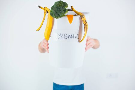 Young man isolated over white background. Guy hold bucket with organic waste inside in front himself. Sorting and recycling time. take care about environment.の写真素材