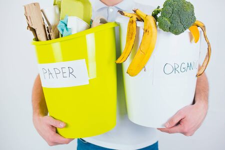 Young man isolated over white background. Cut view and close up of hands holding buckets with separated organic and paper waste ready for recycling.の写真素材