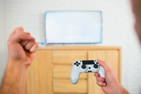 Young man sit in room during quarantine. Cut view of guy holding joystick in one hand and fist with...