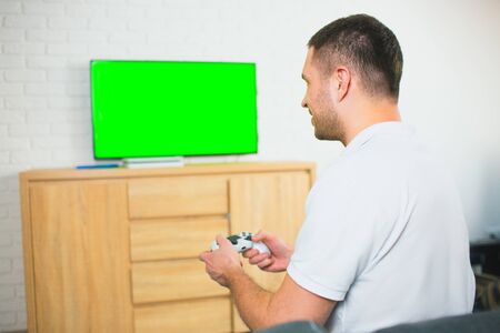 Young man sit in room during quarantine. Guy playing games alone using joystick or gamepad. Green...